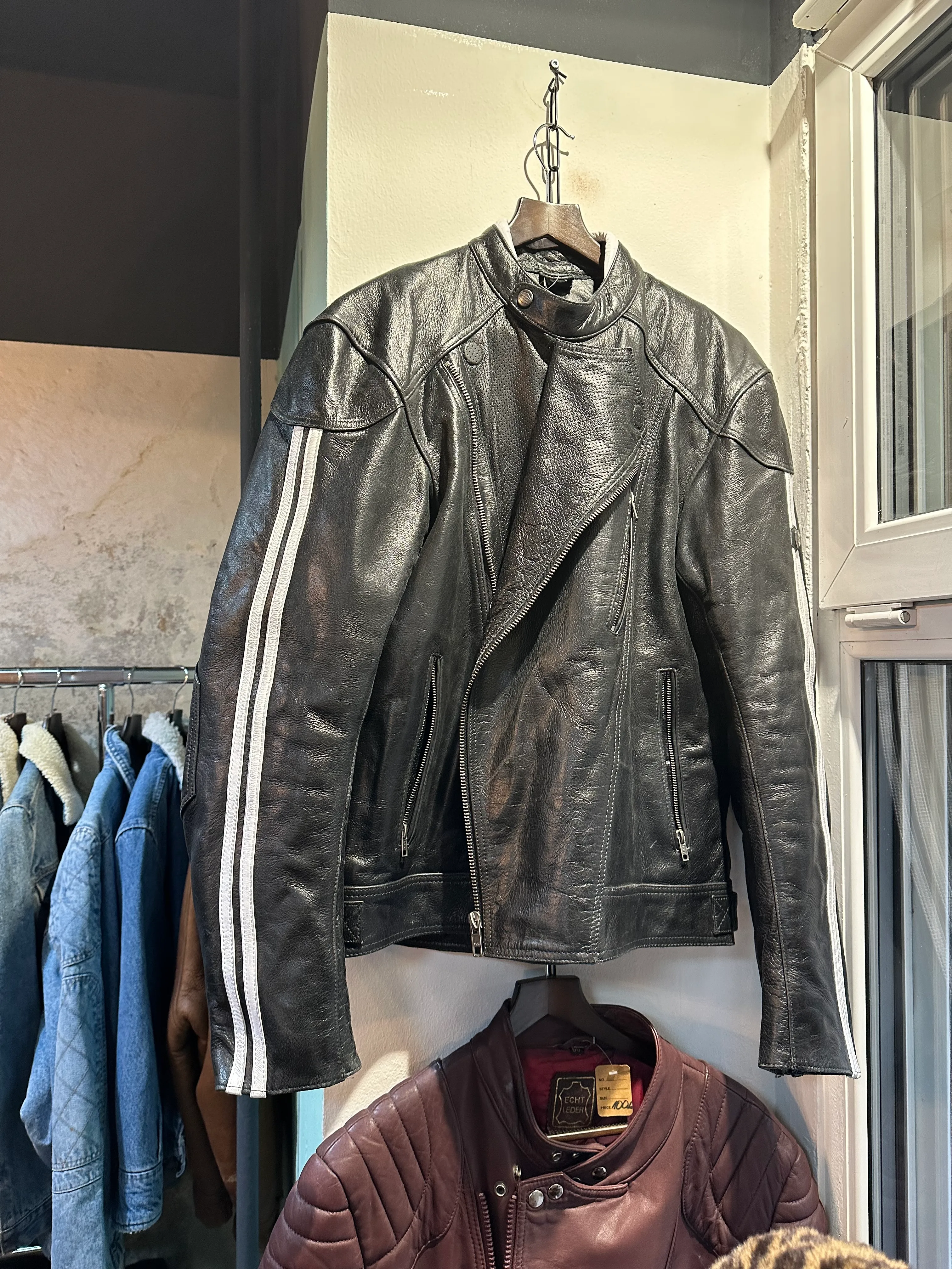 Schwarze Vintage-Motorradjacke aus Leder mit weißen Streifen bei Ava Vintage in Neukölln
